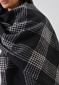 Zwart-wit geblokte sjaal gemaakt van zachte, textuurrijke stof, met een groot, warm ontwerp dat comfortabel over de schouders hangt.