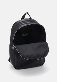Black backpack with a smooth, durable exterior. Features vertical stripes, a front zip pocket, and a spacious open interior.