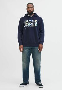 Mørkeblå hættetrøje med "JACK & JONES" logo i farverige bogstaver, paired med lyse denim jeans og sorte sneakers.