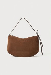 Brown suede shoulder bag with a curved shape, thin leather strap, and a small zip closure. Notable branding in gold at the bottom.