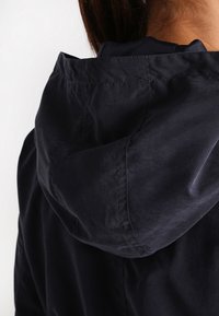 Navy blue hooded jacket featuring a textured fabric, visible stitching details, and a softly contoured hood design.