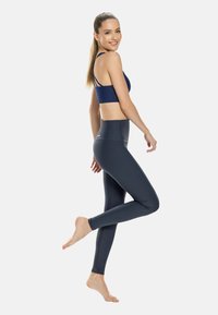 Sujetador deportivo azul marino con tirantes finos, combinado con leggins de talle alto en gris oscuro. Tela suave y elástica con un diseño ajustado.