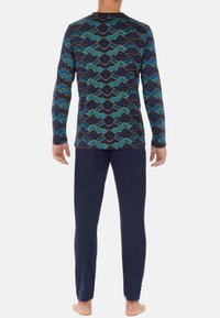 Langärmliges Oberteil mit abstraktem Wellenmuster in Blau und Gelb auf dunklem Hintergrund, kombiniert mit marineblauen Hosen; weicher, elastischer Stoff.