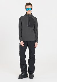 Grauer langärmeliger Zip-Hoodie mit einer schwarzen Tasche, kombiniert mit schwarzen Hosen und schwarzen Skischuhen. Wird durch eine blaue Sonnenbrille ergänzt. Glatte Textur.