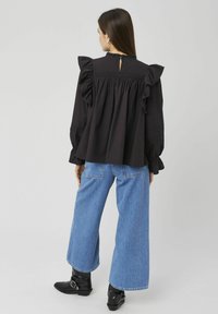 Blouse noire à manches volantées et dos échancré, associée à un jean bleu à jambes larges et des bottines noires.