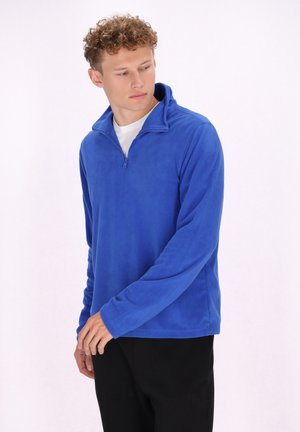 Felpa blu in pile con colletto alto e zip frontale. Tessuto morbido, maniche lunghe e vestibilità comoda. Abbinata a pantaloni neri.