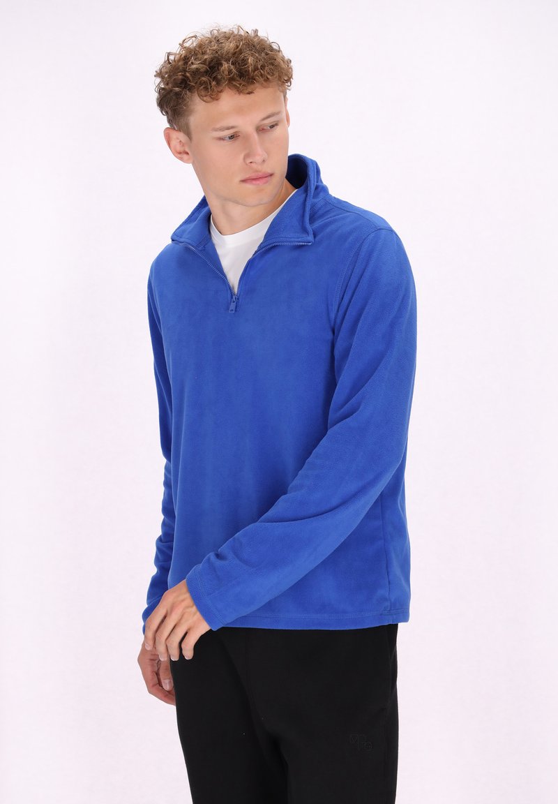 Felpa blu in pile con colletto alto e zip frontale. Tessuto morbido, maniche lunghe e vestibilità comoda. Abbinata a pantaloni neri.