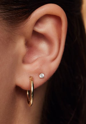 Goldohrringe und ein kleiner Zirkonia-Stecker im Ohrläppchen. Nahaufnahme zeigt die Ohrstruktur und die Details des Schmucks.