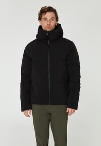 Chaqueta acolchada negra con un alto cuello, cierre de cremallera frontal y dos bolsillos laterales. Presenta una tela texturizada y un ajuste relajado.