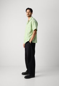Green short-sleeve shirt with sun pattern, black loose-fitting pants, and black shoes. The shirt features a collar and button details.