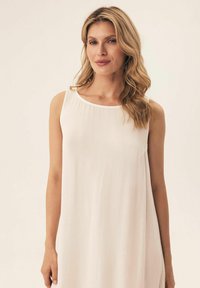 Beżowa sukienka bez rękawów z okrągłym dekoltem, uszyta z fakturowanej tkaniny, swobodnie opada z ramion, tworząc luźną sylwetkę.