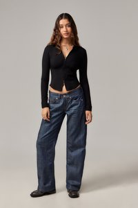 Juodas ilgomis rankovėmis trumpas viršus su užtrauktuku priekyje, derinamas su laisvais mėlynais džinsais su klasikinėmis penkiomis kišenėmis.