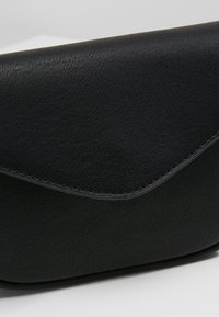 Clutch in pelle nera con una texture liscia, chiusura a linguetta angolare e bordi cuciti. Design semplice e pochi dettagli in metallo.