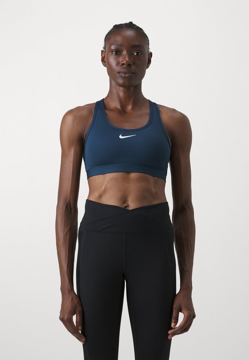 Soutien-gorge de sport bleu marine avec un design dos nageur et un logo blanc. Associé à un legging noir taille haute, offrant une texture lisse et une coupe ajustée.