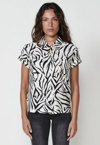 Camisa de botones de manga corta con un patrón de cebra en blanco y negro, hecha de tejido ligero, con dos bolsillos en el pecho y un cuello.
