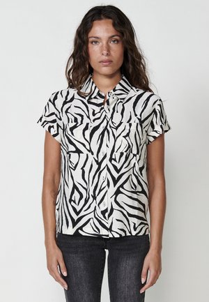 Camisa de botones de manga corta con un patrón de cebra en blanco y negro, hecha de tejido ligero, con dos bolsillos en el pecho y un cuello.