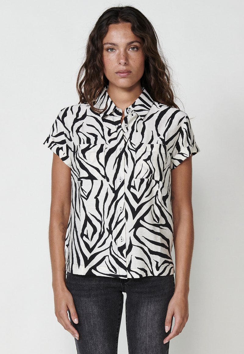 Camisa de botones de manga corta con un patrón de cebra en blanco y negro, hecha de tejido ligero, con dos bolsillos en el pecho y un cuello.