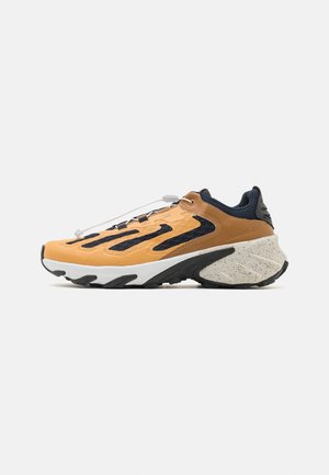 Scarpa sportiva bassa marrone chiaro e nera con suola spessa screziata e pollice al tallone, mostrata di lato su sfondo bianco.