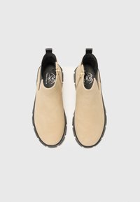 Botas de tobillo beige hechas de ante, con una textura suave, suela de goma negra y cremalleras laterales para facilitar su uso.