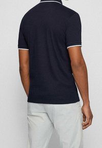 Polo shirt blu navy con bordini bianchi al colletto e alle maniche. Maniche corte e orlo dritto, realizzato in un morbido tessuto misto cotone.