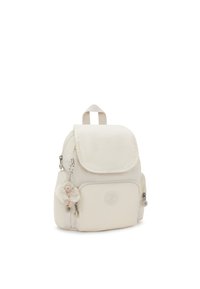 Mochila mini de tela color crema con solapa, bolsillo delantero y charm de peluche. Cuenta con herrajes metálicos y un logo de marca circular grabado.