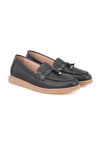 Zwarte geperforeerde leren loafers met een tan rubberen zool, voorzien van een decoratieve band en metalen accent aan de voorkant.