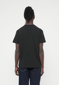 Μαύρο κοντομάνικο μπλουζάκι με στρογγυλή λαιμόκοψη. Κατασκευασμένο από υφασμάτινο υλικό με υφή, η πίσω πλευρά είναι απλή χωρίς στολίδια. Συνδυασμένο με μπλε τζιν.