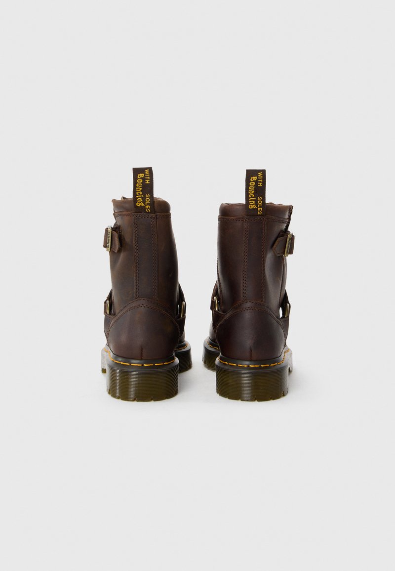 Bottines en cuir marron avec un bout arrondi, détail de boucle sur le côté et surcoutures jaunes renforcées. Présente une languette jaune et une semelle épaisse.
