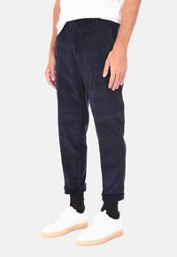 Pantaloni in corduroy blu navy con una vestibilità affusolata, dotati di tasche frontali e orli risvoltati, abbinati a sneakers bianche e calzini neri.
