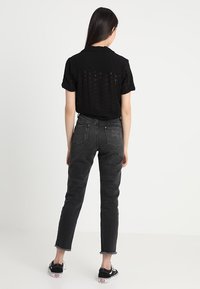 Maglietta nera a maniche corte con design a occhio, abbinata a jeans grigi a vita alta e strappati. Calzature: scarpe da ginnastica nere con dettagli bianchi.