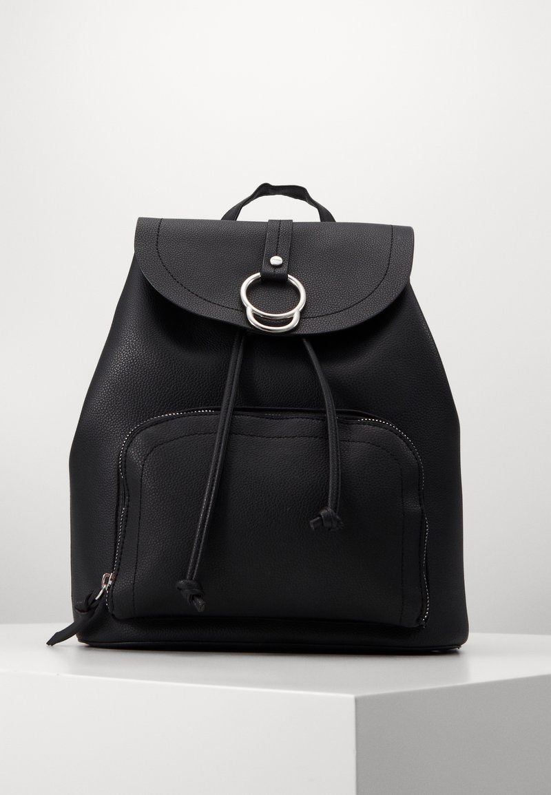 Sac à dos en cuir noir avec une poche avant zippée, une fermeture à cordon, un rabat sécurisé par une boucle en anneau argentée et une poignée supérieure.
