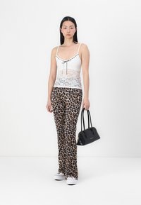 Haut en dentelle avec des fines bretelles et un détail en nœud, associé à un pantalon imprimé léopard et un petit sac à main noir, porté avec des baskets blanches.