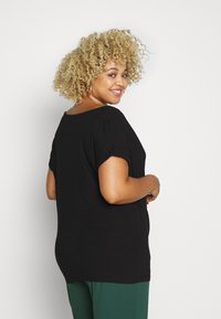 Sort t-shirt med korte ærmer, afslappet pasform, rund halsudskæring og blødt stof, kombineret med grønne bukser, set fra ryggen.