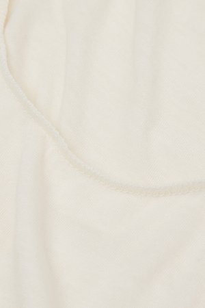 Krämfärgat tyg med en mjuk, slät textur och en diskret glans. Kanterna visar en fin, delikat sömnadsdetalj.