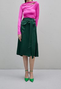 Rosa långärmad topp med utskärningsdetalj, matchad med en grön A-linjeskirt med en rosett och banden, kompletterad med gröna spetsiga klackar.