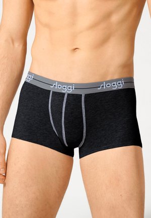 Torso maschile che indossa boxer neri con una fascia grigia con il marchio "sloggi" su uno sfondo chiaro e semplice.