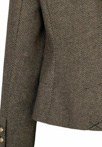 Tissu marron et noir à motif chevrons sur une manche et un côté de veste, montrant des boutons dorés sur le poignet.