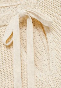 Jasno kremowy sweter dziergany z teksturowanym wzorem i wiązanym detalem z tkaniny przy dekolcie.