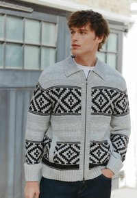 Grå og sort mønstret lynlåstrøje med krave, med geometriske design. Strikket tekstur og ribbede manchetter.