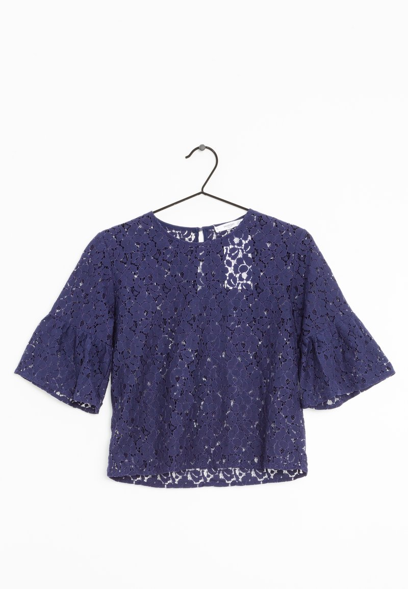 Blouse en dentelle bleu marine avec motif floral, manches mi-longues, col rond et coupe ample, suspendue sur un cintre noir.
