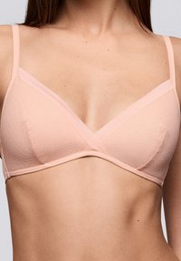 Gevulde, lichtroze bralette met driehoekige cups en dunne verstelbare bandjes. Glad, rekbaar materiaal met subtiele textuur langs de randen.