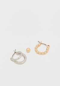 Strieborná náušnica v tvare kruhu a zlatá náušnica s malými guľatými korálkami; jedna zlatá korálka na bielom pozadí.