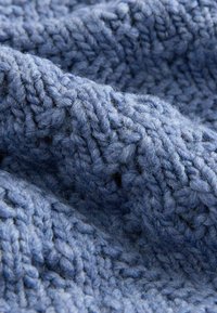 Primer plano de una tela de punto azul con hilo grueso y patrones de puntadas de punto visibles que crean una superficie texturizada y suave.