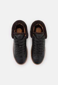 Baskets en cuir noir avec une tige texturée, une bordure en fausse fourrure noire et des semelles en caoutchouc marron, dotées de lacets noirs et d'une doublure intérieure.