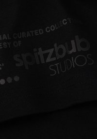 Black fabric with printed text in varying shades of grey. Reads "spitzbub STUDIOS" and "curated collection" along with patterns and logos.