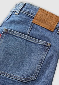 Poche arrière d'un jean en denim bleu avec une étiquette en cuir marron Levi's cousue au-dessus et une petite étiquette rouge Levi's sur le côté de la poche.