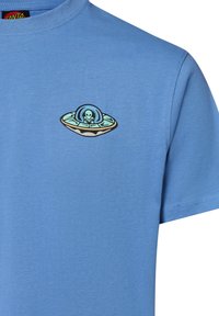Lichtblauw t-shirt van katoen met een grafisch ontwerp van een UFO met een alien, geplaatst op de linkerborst. Korte mouwen en ronde hals.