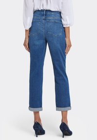 Mörkblå denimjeans med rak benform, utrustade med uppvikta fållar och två bakfickor, kombinerade med högklackade skor.