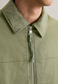Hellgrüne Jacke mit einem weichen Cordkragen, Reißverschluss vorne und strukturiertem Stoff. Verfügt über einen dekorativen Ziehstreifen und Steppdetails.