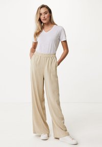 Pantalons larges beige en matériau doux, avec une taille élastique, assortis à un t-shirt blanc à col en V et des baskets blanches.
